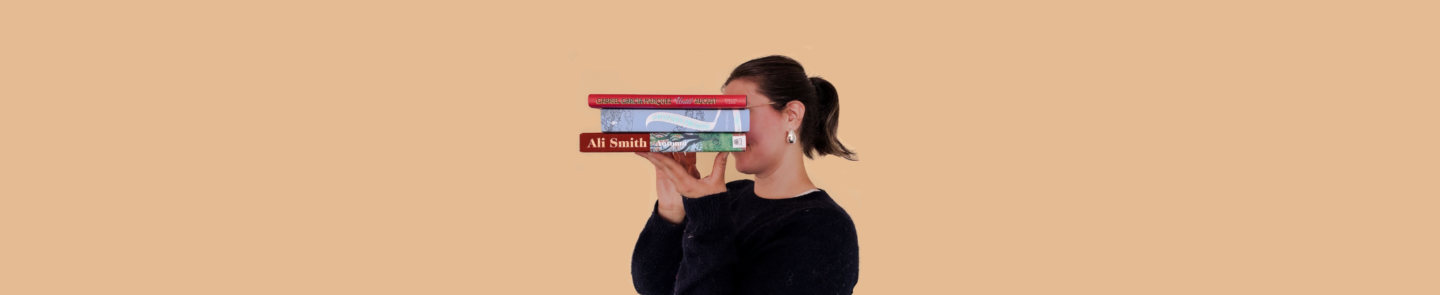 girl in a blue jumper holding a stack of three books in front of her face